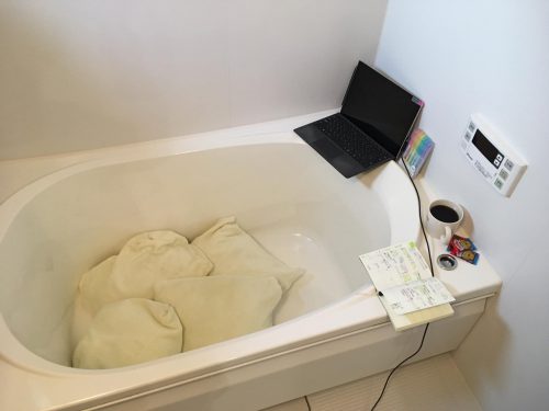 お風呂場のバスタブにパソコンやスマートフォンを持ち込んで作業スペースにしている様子